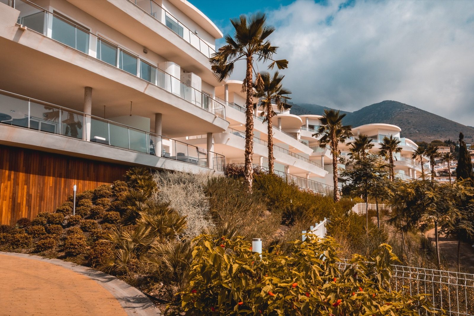 Terraced white apartments above a flowering hillside garden, mountains beyond